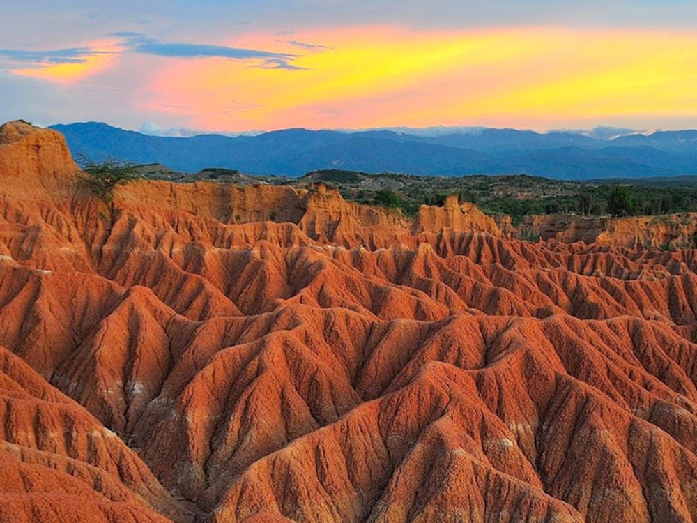 Formaciones arcillosas rojizas del Desierto de la Tatacoa al atardecer, con cárcavas profundas, vegetación dispersa y cielo multicolor