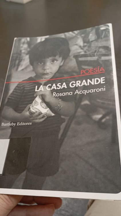 Portada del libro "La casa grande" de Rosana Acquaroni, que incluye a 'La destrucción y el amor'. La imagen muestra una fotografía en blanco y negro de un niño con camiseta de rayas oscuras y claras, sosteniendo un paquete
