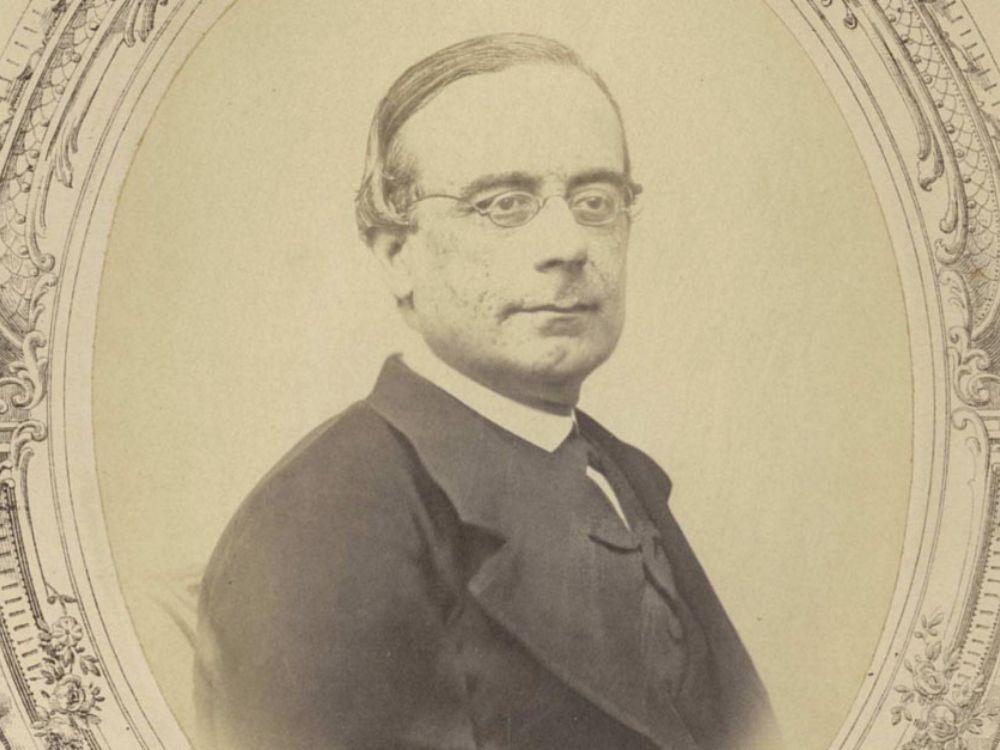 Eduardo Benot. RAE Fotografía histórica en sepia de Eduardo Benot Rodríguez, hombre con gafas redondas, peinado pulcro y vestido formal del siglo XIX, con un marco ornamental alrededor