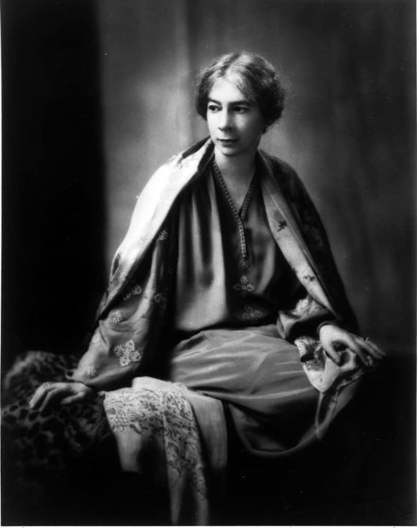 Llegarán suaves lluvias. Retrato en blanco y negro de Sara Teasdale sentada, con expresión serena y vestimenta bordada, sobre fondo oscuro