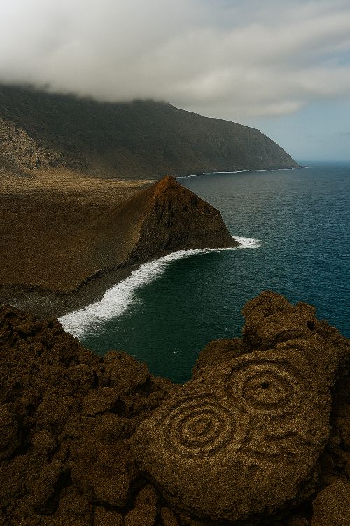Vista panorámica de la costa volcánica de El Hierro con acantilados abruptos y petroglifos aborígenes en primer plano