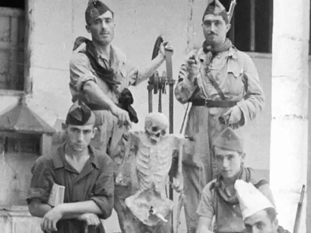 Chiribis. Fotografía histórica en blanco y negro de un grupo de milicianos posando junto a un esqueleto humano sostenido macabramente, como si fuera una figura más del grupo