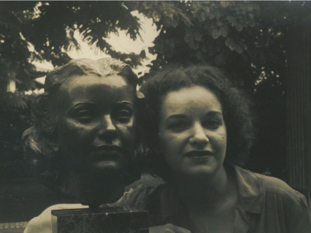 Motivo bañado de luna. Fotografía en blanco y negro de Stella Sierra junto a un busto escultórico que representa su rostro, en un entorno natural