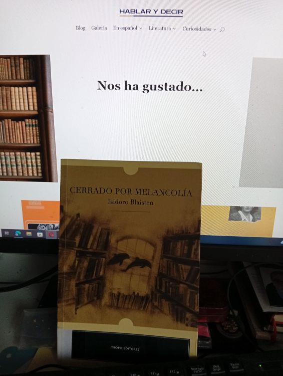 Libro 'Cerrado por melancolía', de Isidoro Blaisten apoyado frente a una pantalla con la página web literaria hablarydecir.com abierta