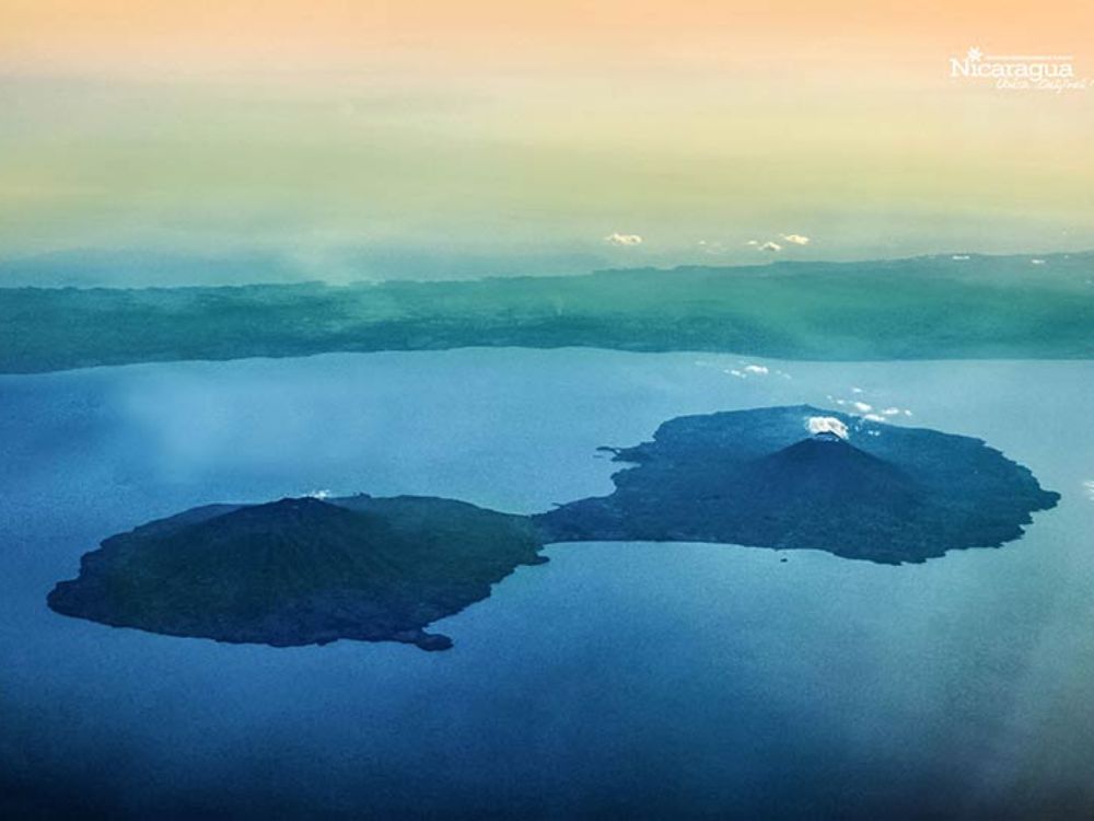 Vista aérea de la Isla de Ometepe con sus dos volcanes emergiendo del Lago Cocibolca al amanecer, bajo un cielo que pasa del naranja al azul