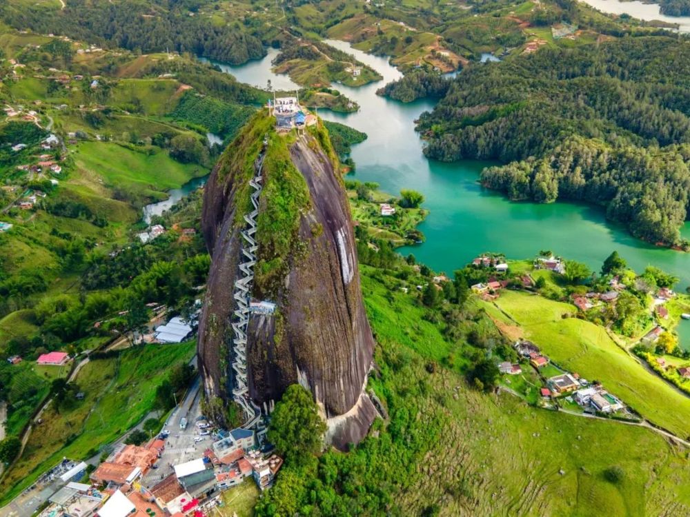 Peñón de Guatapé Vista del Peñón de Guatapé con su escalera zigzagueante incrustada en la roca y el embalse de aguas turquesas extendiéndose entre colinas verdes al fondo