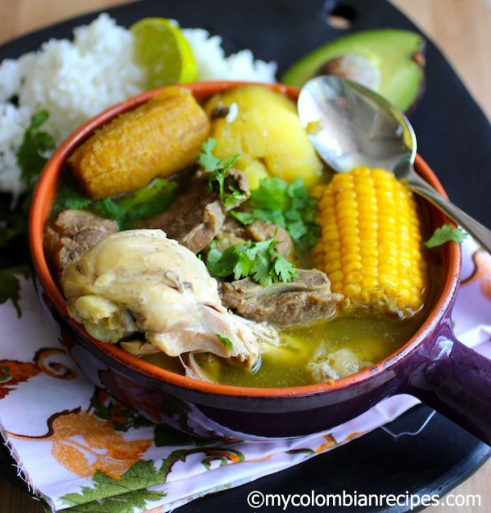 Sancocho trifásico Plato de sancocho trifásico colombiano servido en cuenco rústico con pollo, res, cerdo, mazorca, tubérculos y guarniciones típicas como arroz, aguacate y lima