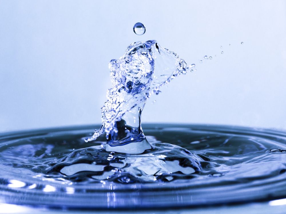 Gota de agua dulce cayendo sobre una superficie líquida, formando una salpicadura circular y un pequeño rebote en forma de gota suspendida en el aire