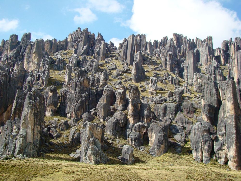 Formaciones rocosas verticales del Bosque de Piedras de Huayllay sobre una ladera cubierta de pasto bajo un cielo parcialmente nublado