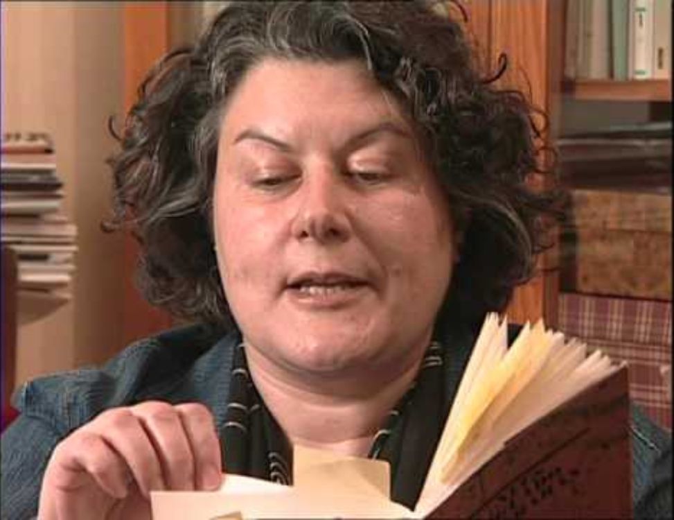 Fama póstuma Neus Aguado, autora de 'Fama póstuma', leyendo un libro en una sala con estanterías llenas de libros y papeles