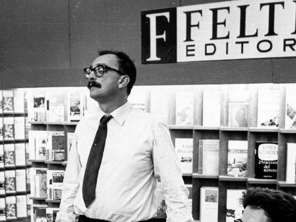 Feltrinelli, de pie frente a estanterías repletas de libros y revistas, bajo un rótulo con el nombre de su editorial.