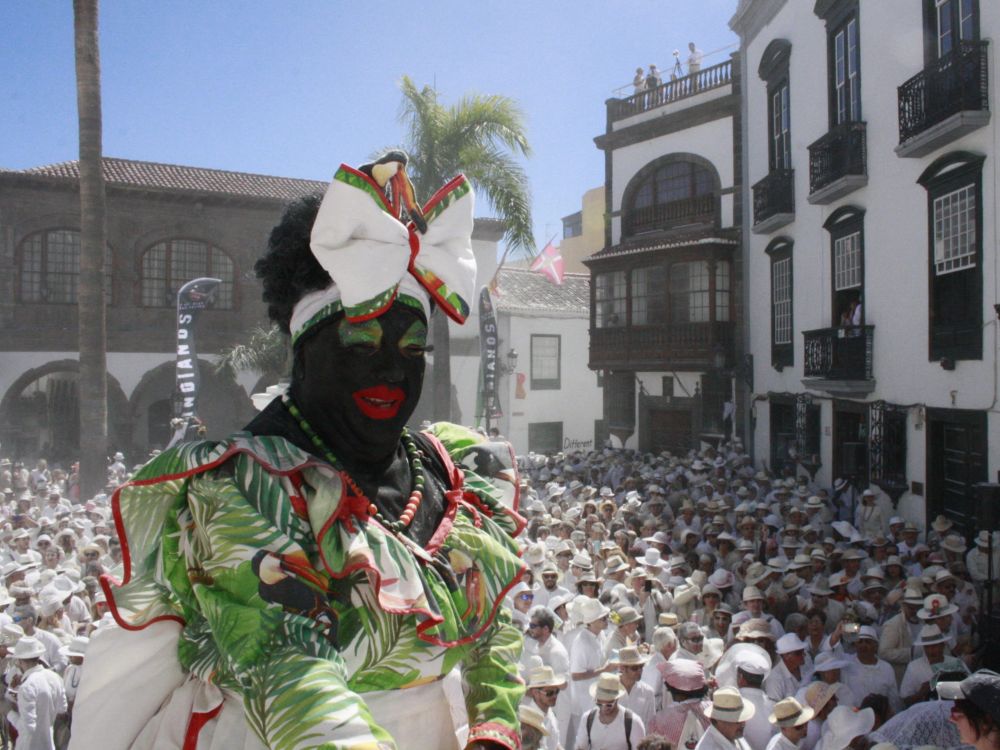 Los Indianos La negra Tomasa rodeada de una multitud vestida de blanco en una plaza de Santa Cruz de La Palma durante la fiesta de Los Indianos