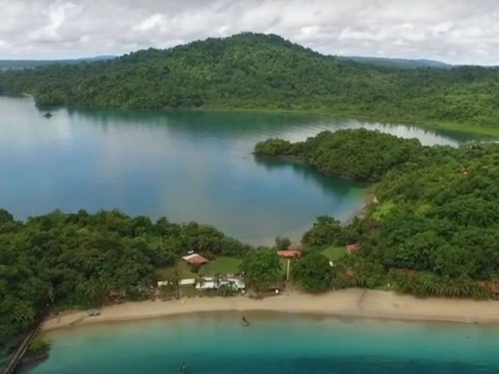 Parque Nacional Coiba Bahía de Coiba con playa de arena clara, aguas turquesas y colinas cubiertas de selva tropical, junto a un pequeño conjunto de edificaciones y un muelle.