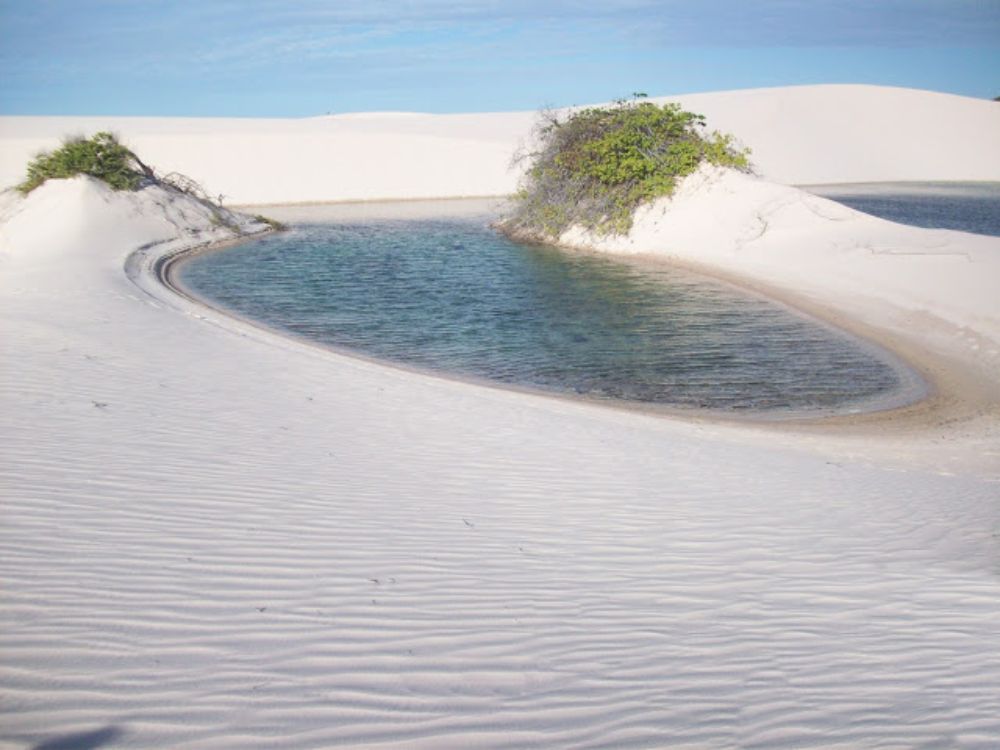 Sábanas Maranhenses. Dunas blancas con una laguna de agua azul‑verdosa entre ellas y pequeños arbustos en la arena