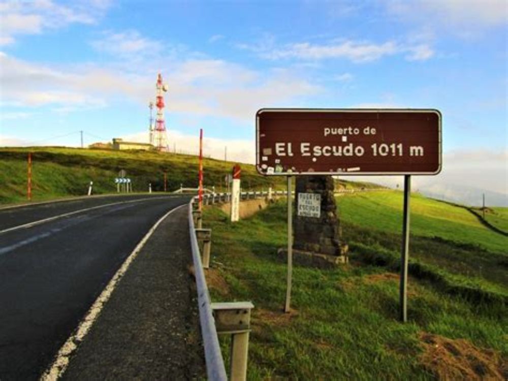 Toma del Puerto del Escudo. Carretera de montaña que asciende al Puerto del Escudo, con el cartel que marca los 1.011 metros de altitud y las laderas donde se desarrollaron los combates de 1937